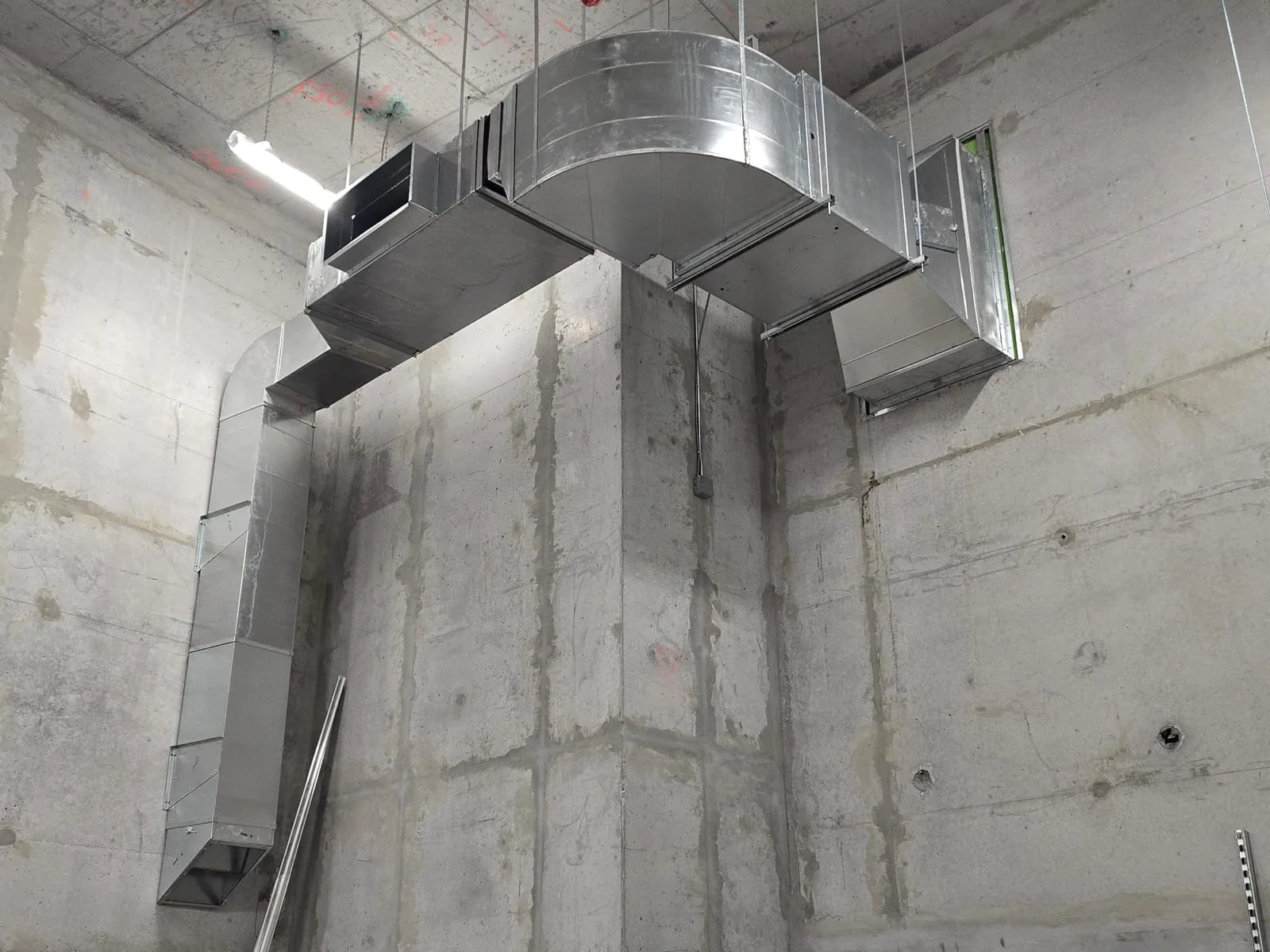 Rigid galvanized rectangular ductwork with a radius elbow and branch takeoffs in an unfinished concrete room