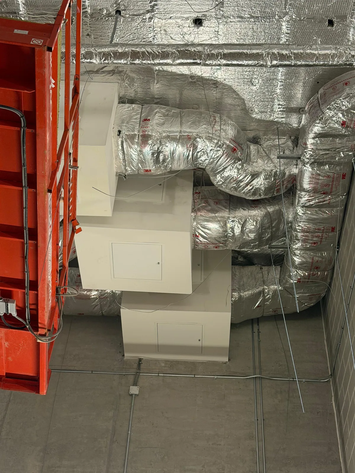 Foil-wrapped flexible duct connections at white equipment cabinets in a concrete mechanical room