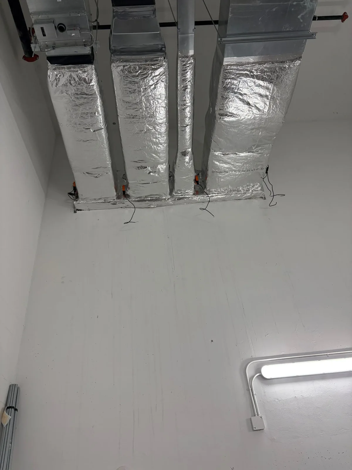 Three vertical foil-wrapped duct drops with motorized dampers in a white mechanical room