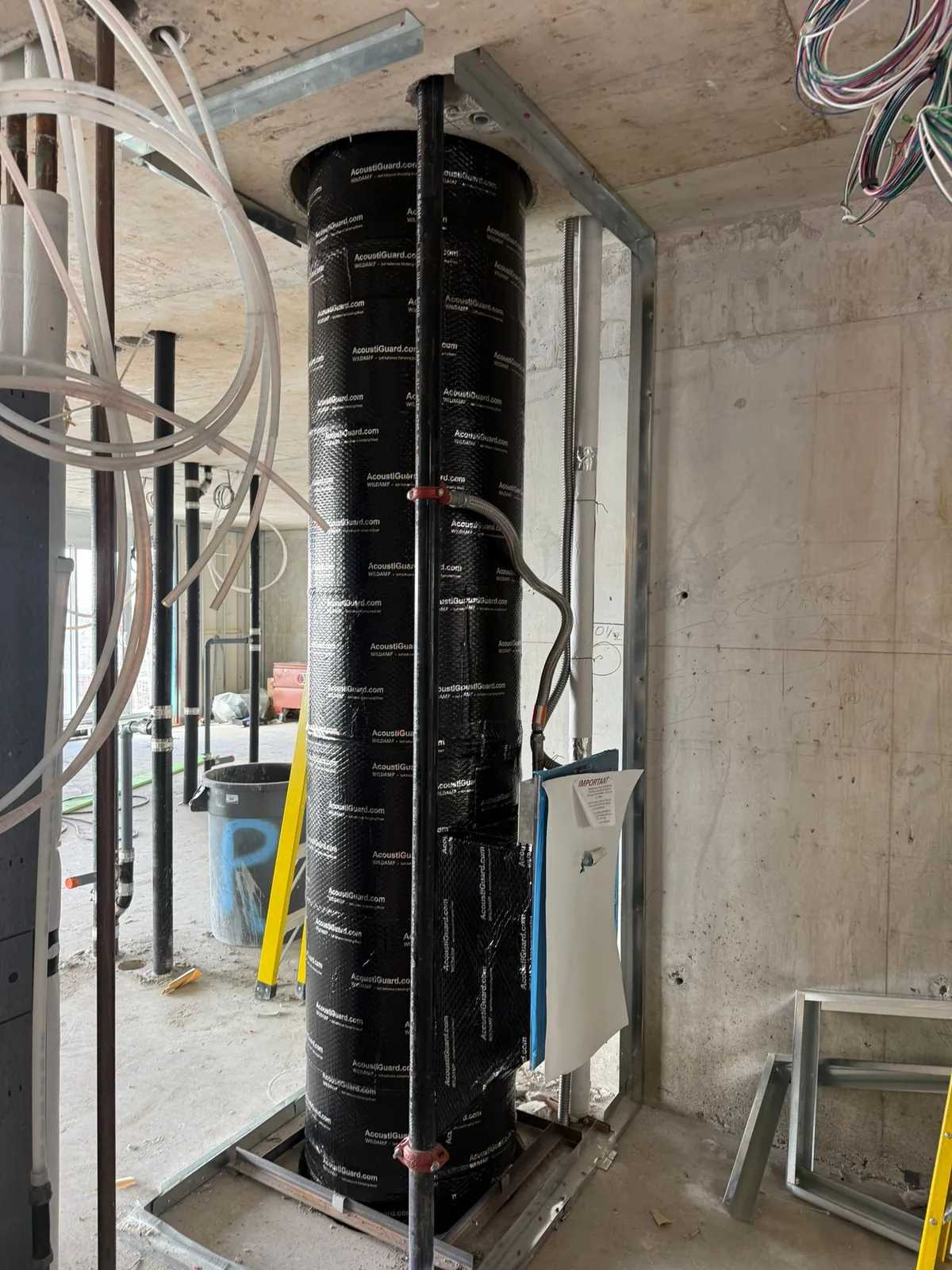 Black AcoustiGuard-wrapped vertical duct riser framed with steel studs on a concrete floor