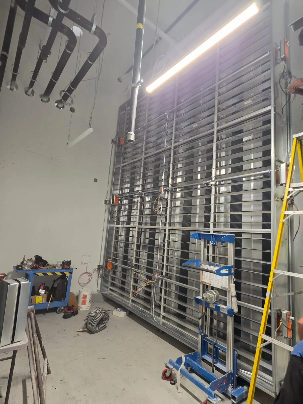Large galvanized damper and louvre wall with actuators above a scissor lift in a concrete room