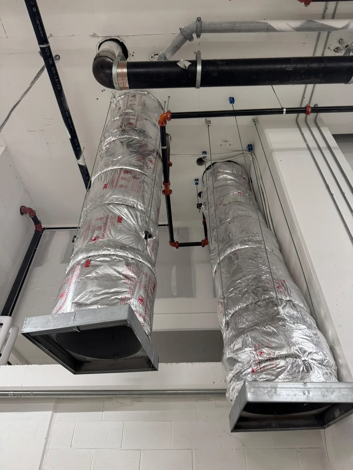 Foil-wrapped horizontal duct runs with fire dampers along a white ceiling beside black pipe