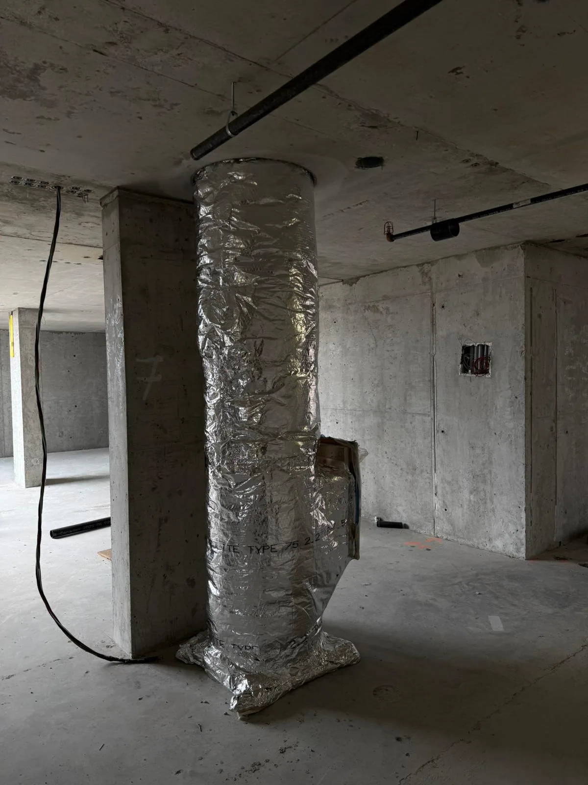 Foil-wrapped vertical duct riser with a control enclosure in a bare concrete high-rise interior