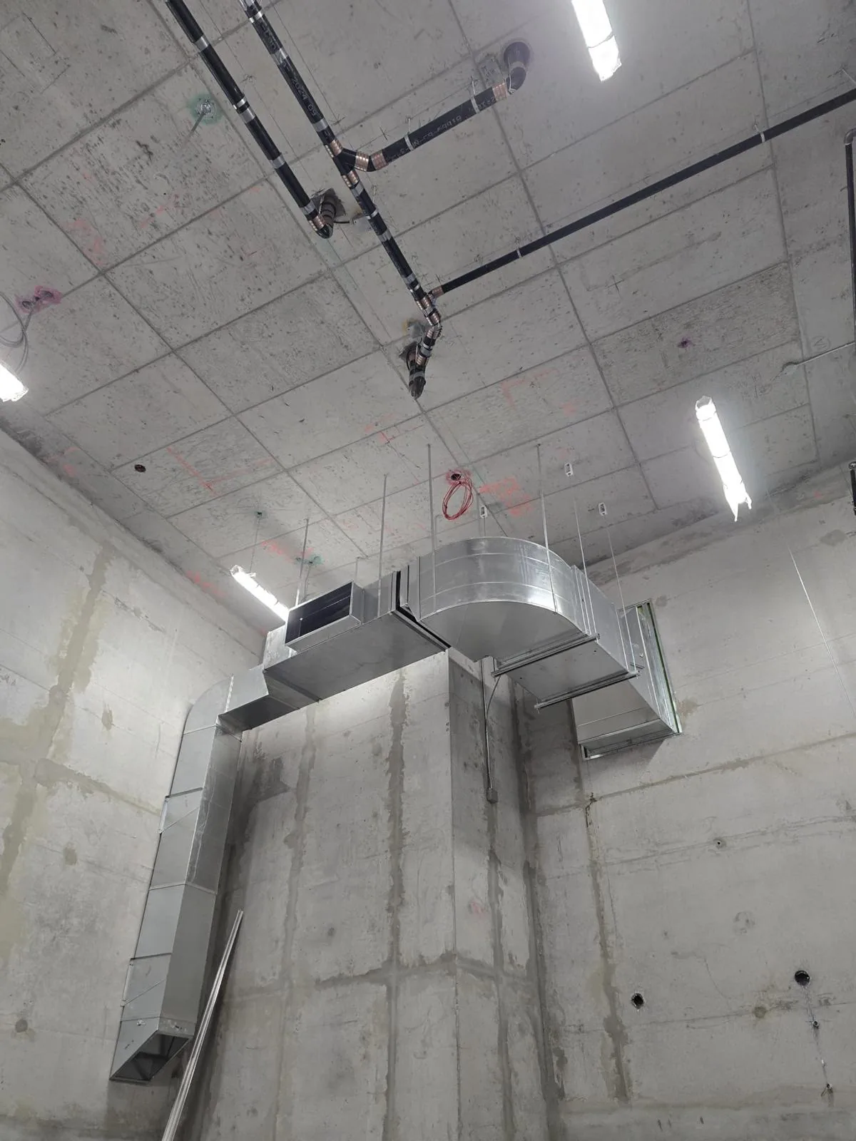 Suspended galvanized duct with a radius elbow hung on threaded rods below a concrete slab