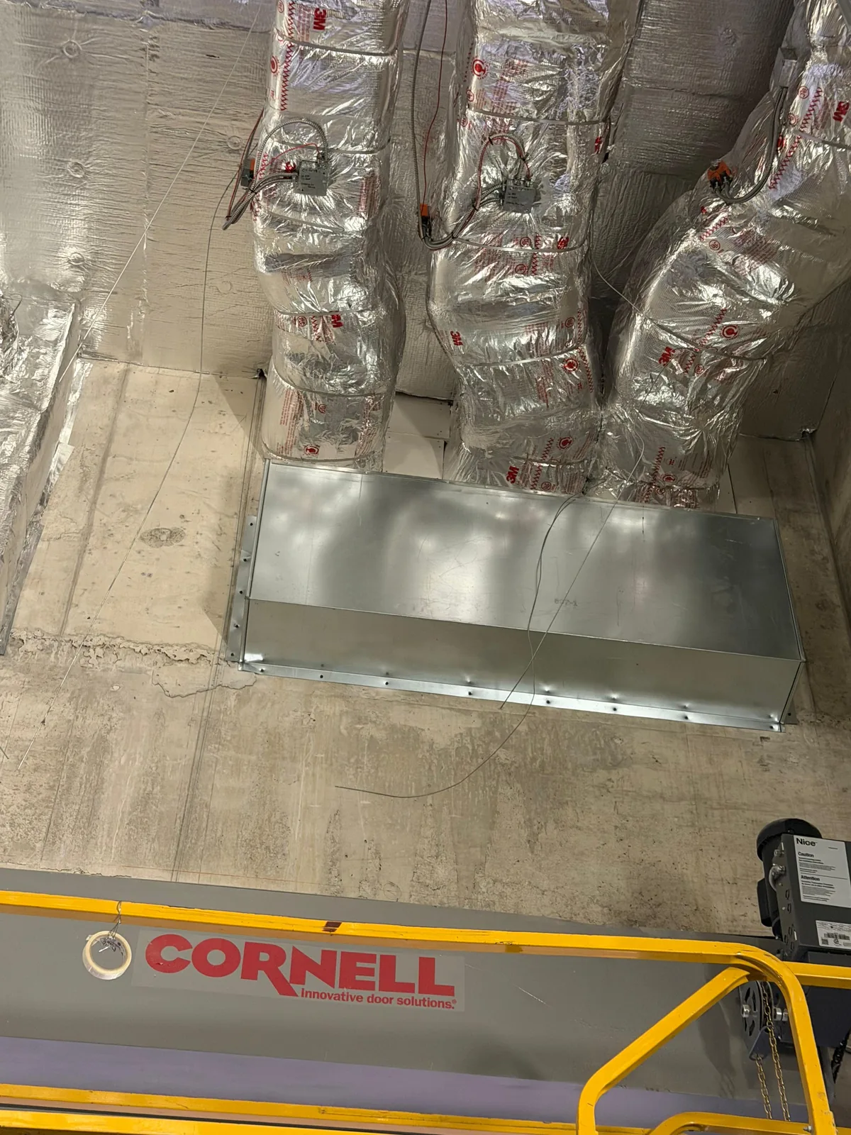 Galvanized rectangular duct with fire dampers installed above a Cornell overhead door