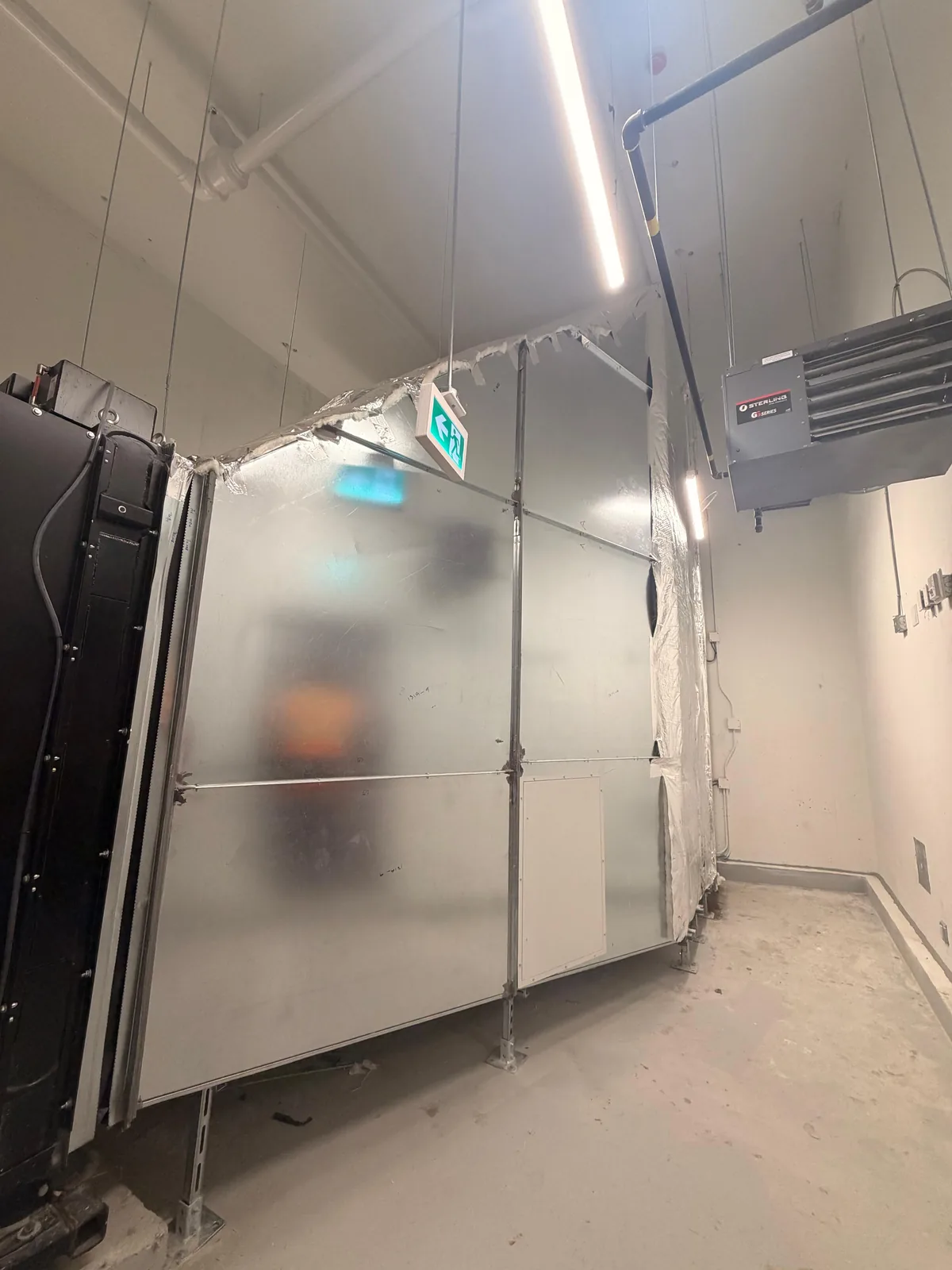 Insulated air handling unit enclosure with louvred panel beside a wall-mounted unit heater