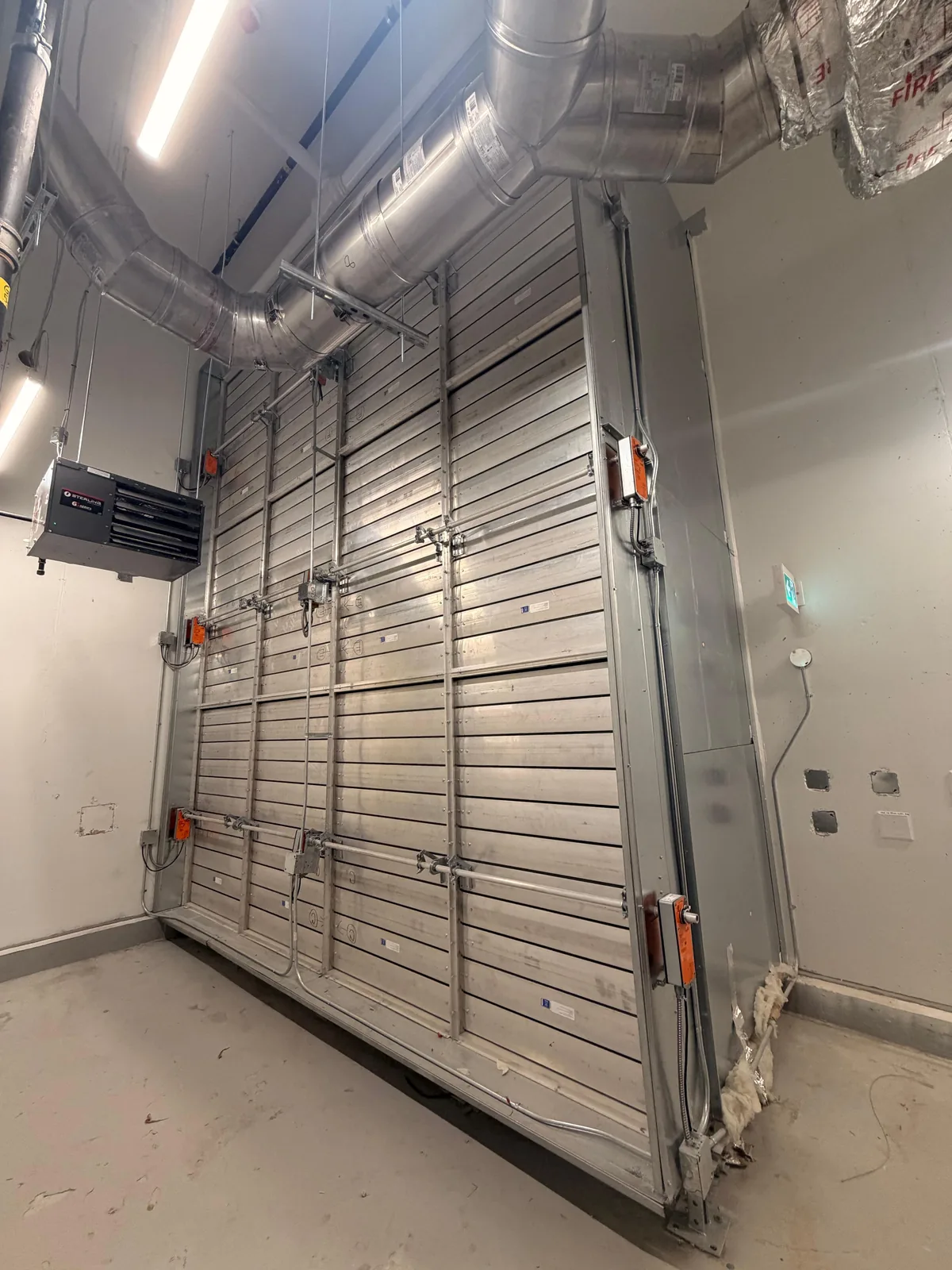 Large galvanized damper bank with actuators below round ductwork and a unit heater