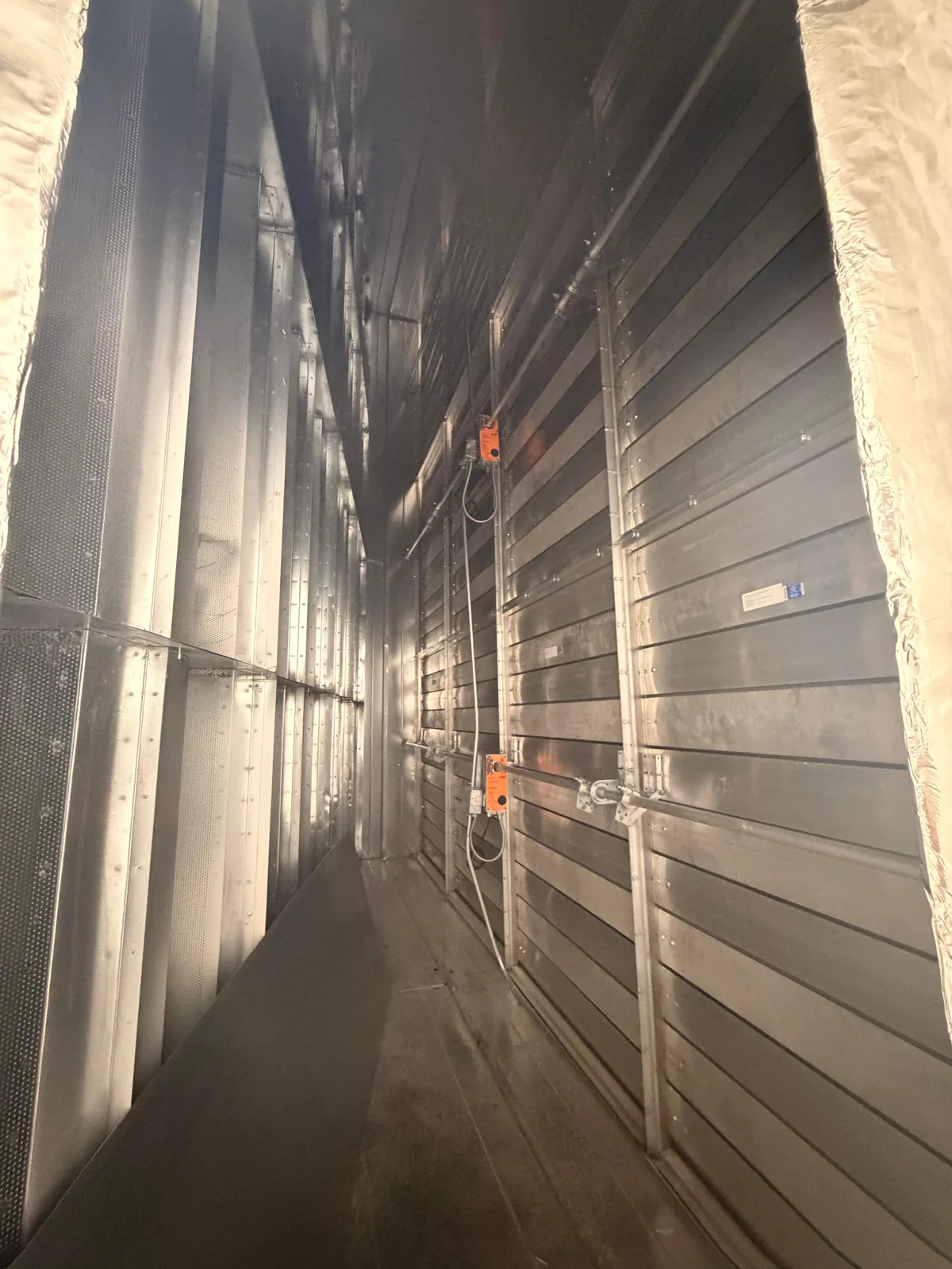 Interior view along a large galvanized duct section lined with perforated metal panels
