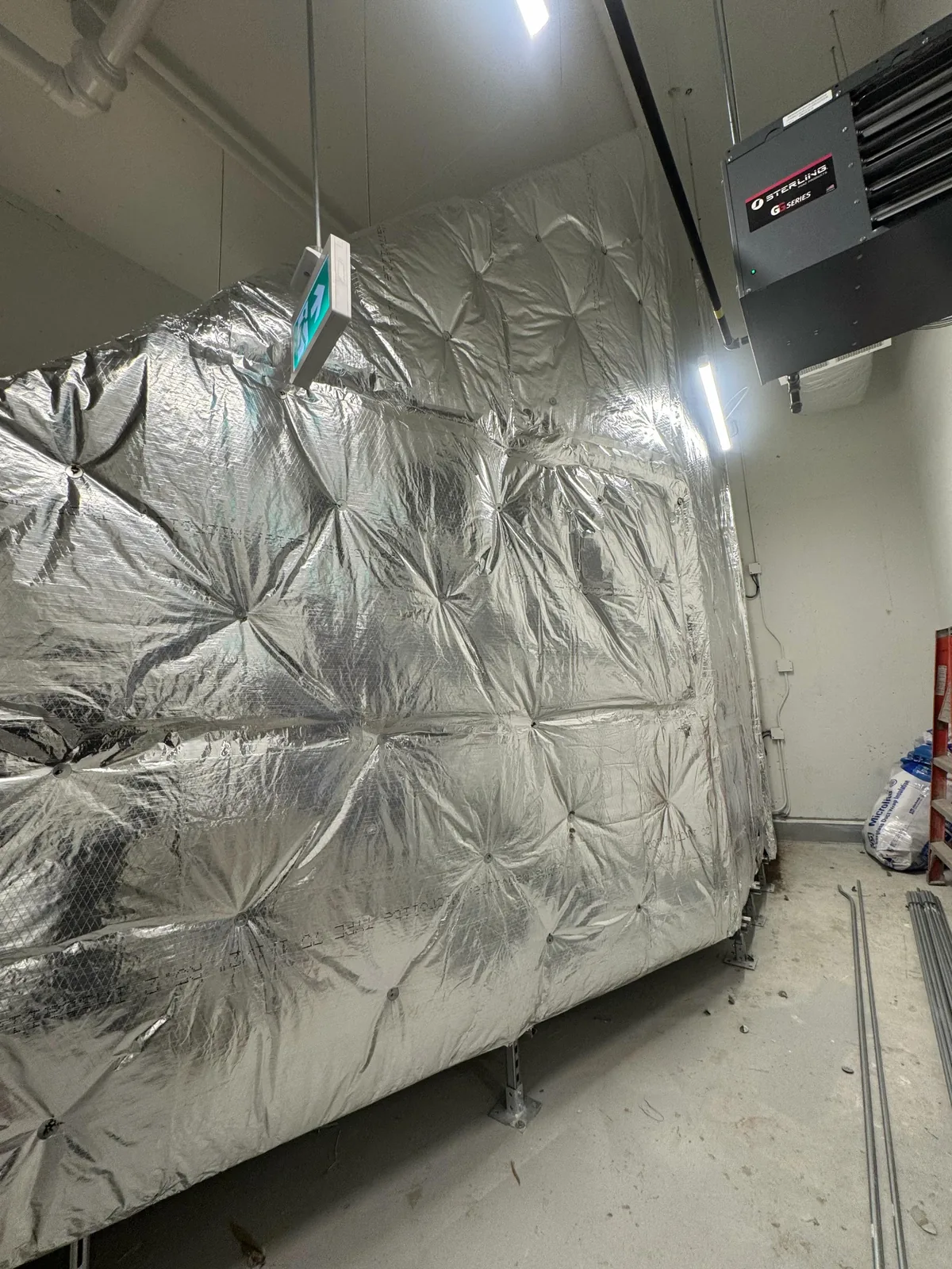 Foil-faced insulated duct plenum wrapped in wire mesh beside a Sterling unit heater